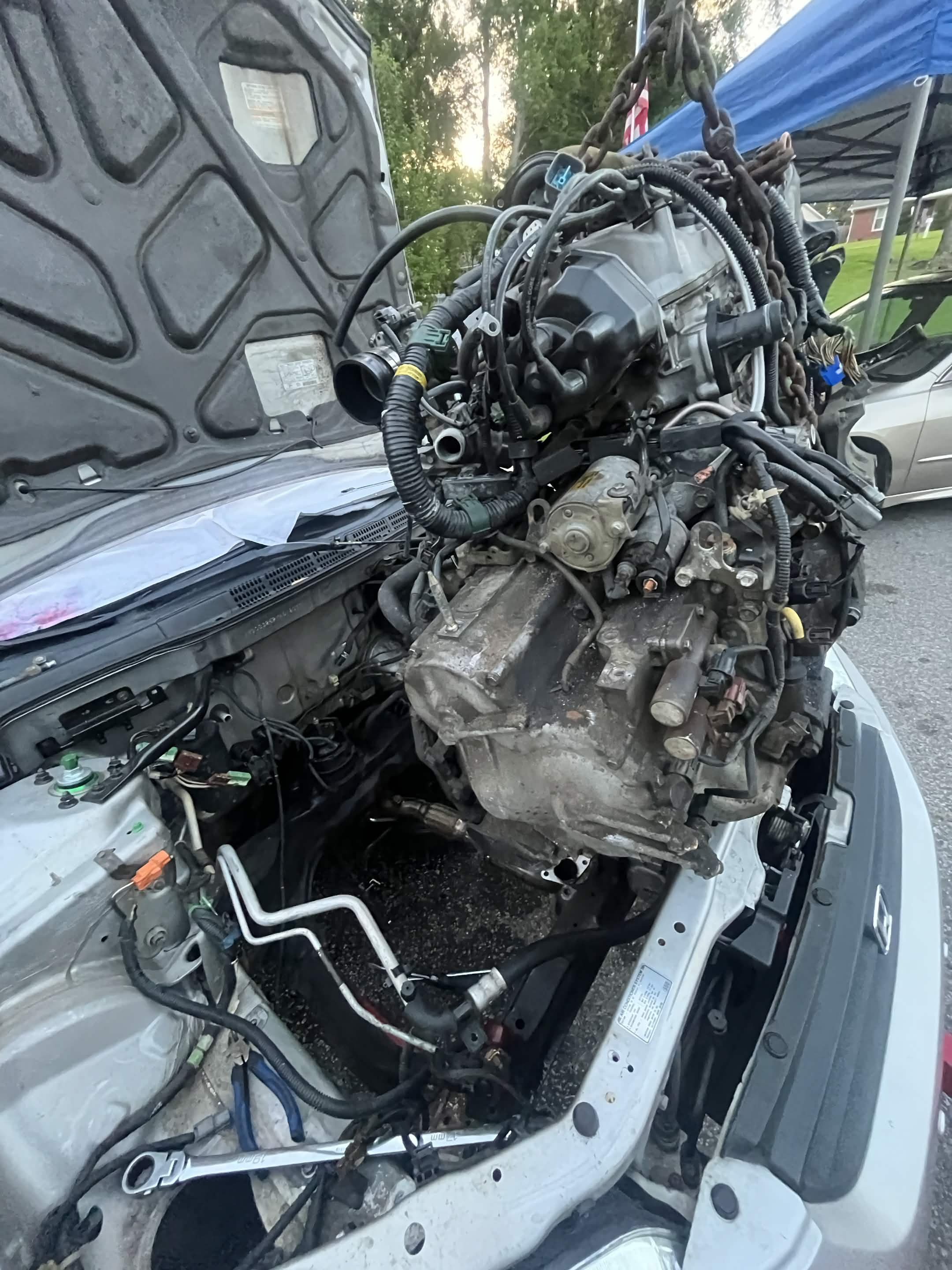 Engine and transmission lifted above an open engine bay during repair work